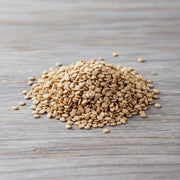 A pile of light brown, oval-shaped grains, possibly rice or lentils, is scattered on a wooden surface.
