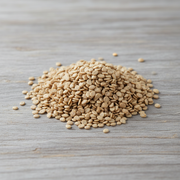 A pile of light brown, oval-shaped grains, possibly rice or lentils, is scattered on a wooden surface.