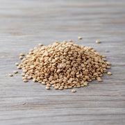 A pile of light brown, oval-shaped grains, possibly rice or lentils, is scattered on a wooden surface.