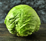 A fresh head of green cabbage sits on a wooden surface against a dark background.