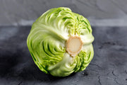 A fresh head of green cabbage with a light brown center is displayed on a dark gray surface.