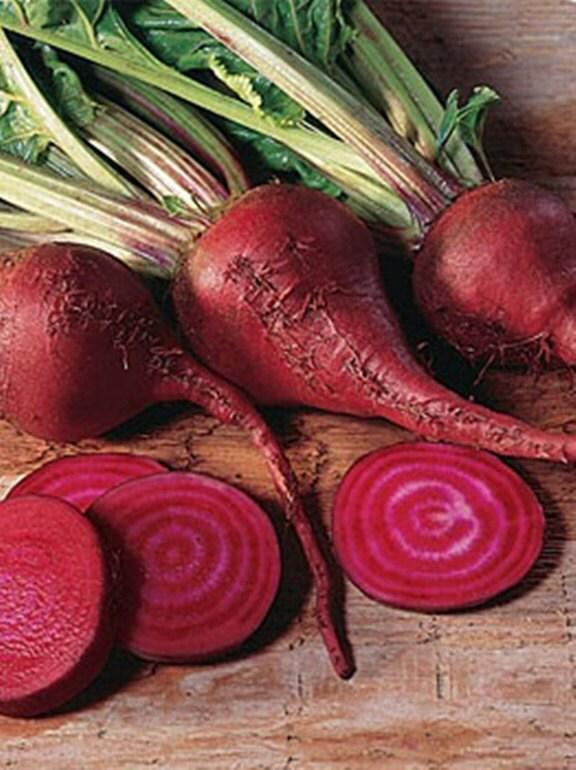 a collection of fresh red beets, including whole and sliced pieces, arranged on a wooden surface.
