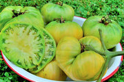 A white bowl filled with green tomatoes, some sliced open to reveal their juicy interiors.