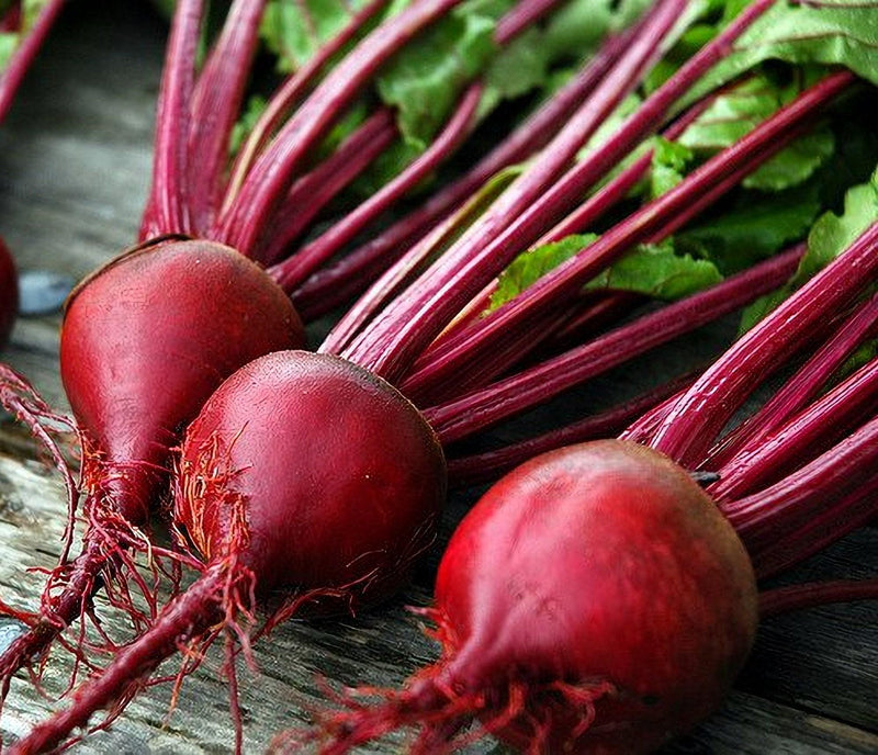 three red beets with long stems, arranged on a wooden surface.