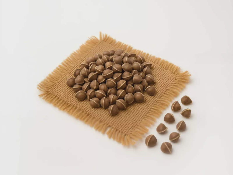 A pile of brown nuts or seeds is arranged on a woven mat or cloth, with some nuts spilling out onto the surface.