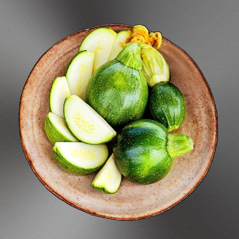 A plate of sliced green zucchini and a whole zucchini are displayed on a brown plate against a gray background.
