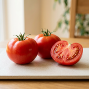 Whole red Ace 55 slicing tomatoes beside a cut half showing meaty flesh