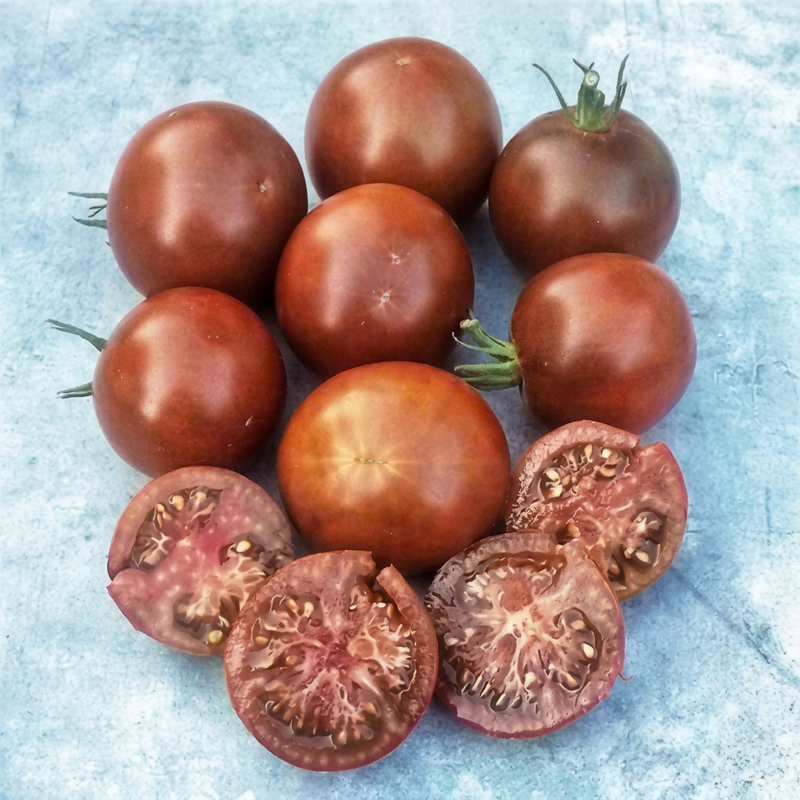 Rounded chestnut-red Carbon tomatoes and juicy cut halves on a pale blue tabletop