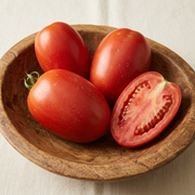 Broad elongated red Amish Paste tomatoes with a cut half showing meaty flesh