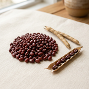 Small red adzuki beans with pale seed scars beside dry tan pods